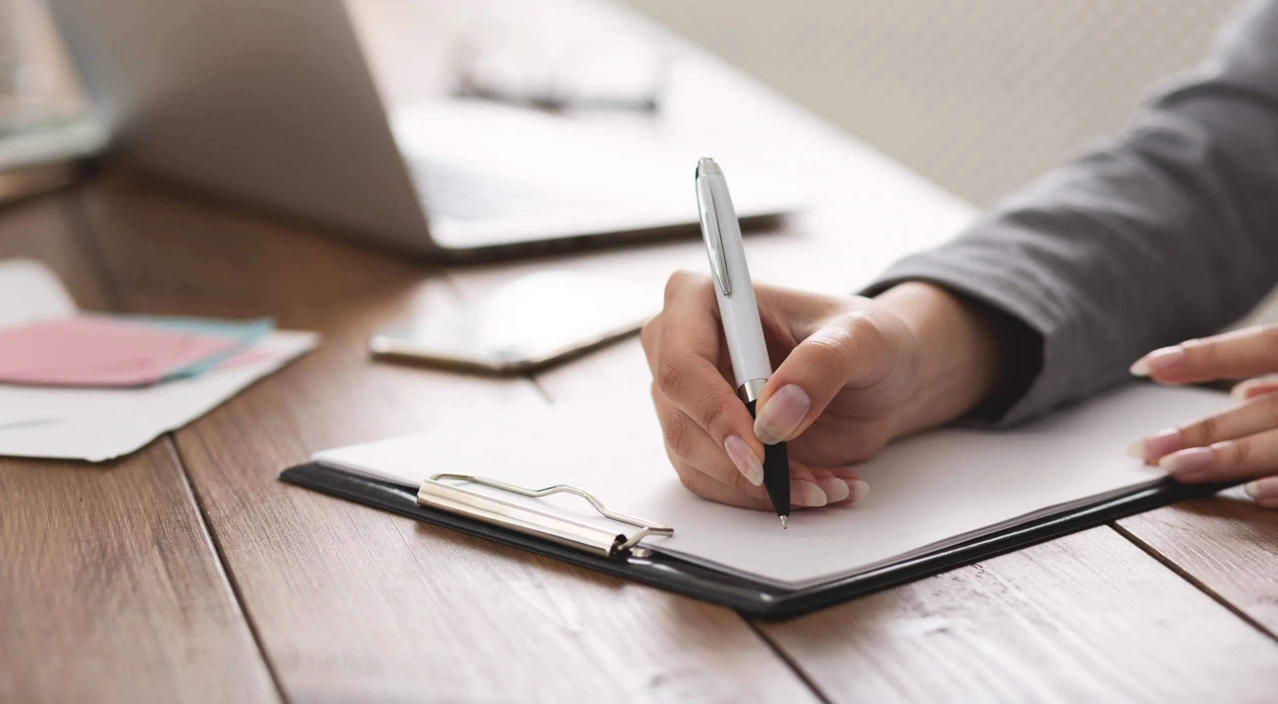 hand holding pen about to write on a piece of paper on a clipboard