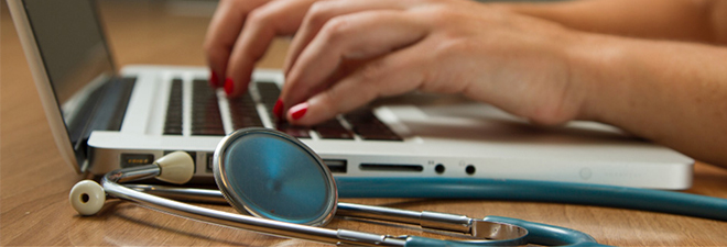 Doctor’s hands on a computer keyboard with medical equipment nearby.