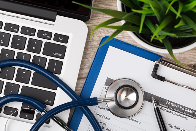 Stethoscope resting on patient information forms beside a laptop on a desk.