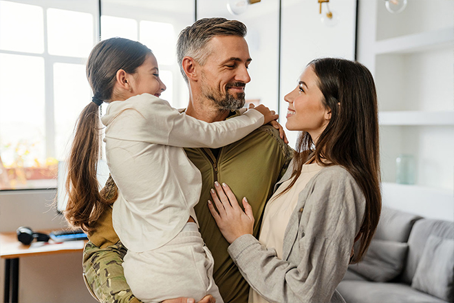 A Veteran in camouflage fatigues embracing his wife and child in a heartfelt reunion.