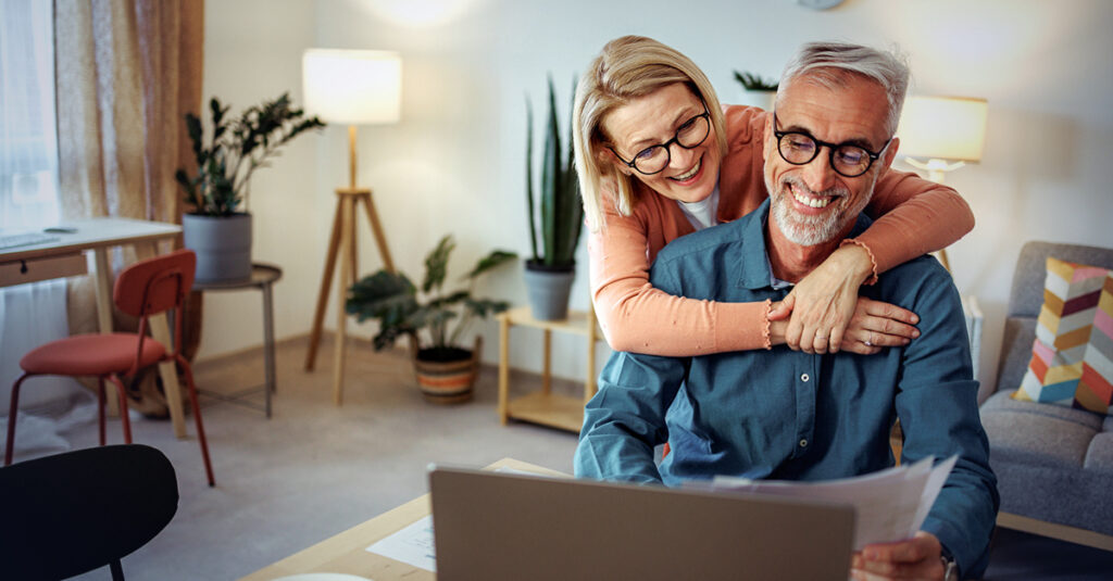 Older couple smiling while reviewing documents on a laptop.
